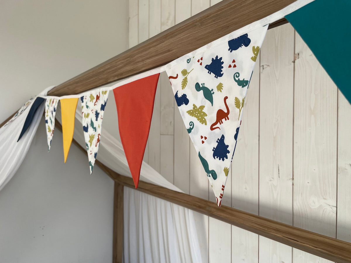Guirlande de 9 fanions en coton fait main qui alterne couleurs unies et imprimés dinosaures, pour décorer une chambre d’enfant 