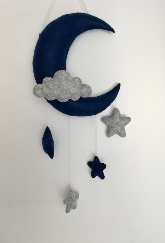 Suspension en feutrine confectionnée à la main composée d’une lune, d’un nuage et quatre étoiles. Couleurs bleu marine et gris chiné 